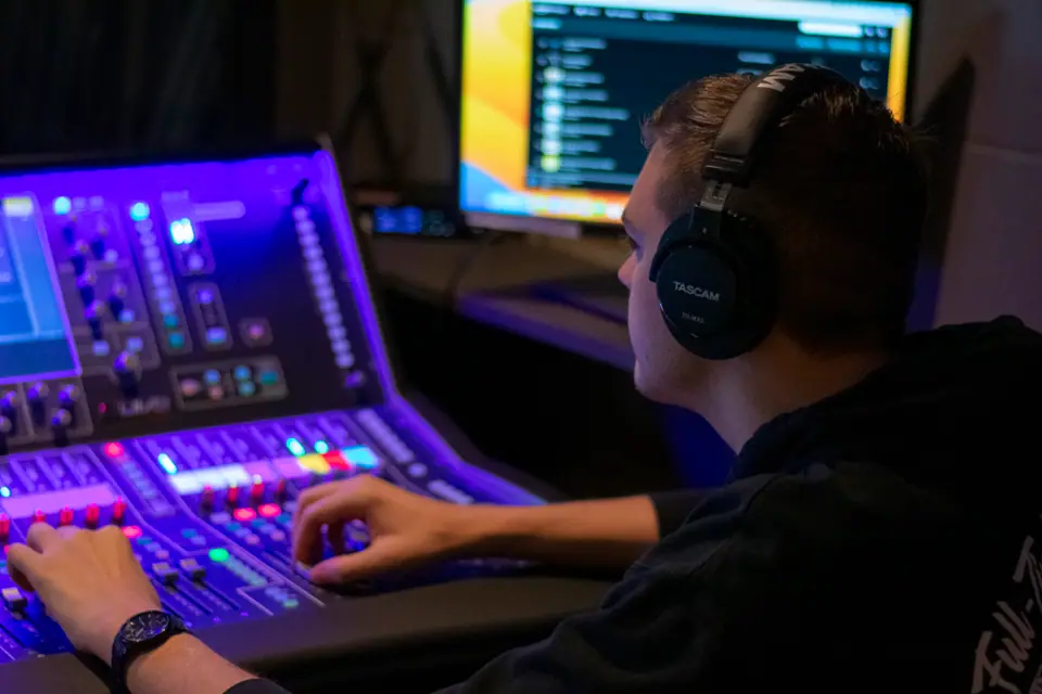 Audio engineer in headphones working a lit mixing console during a live broadcast