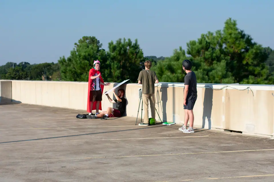 Crew blocking a scene on a rooftop, camera on sticks and an actor lying in position