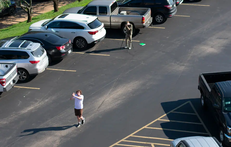 Wide view of a small crew filming an actor across an empty parking lot
