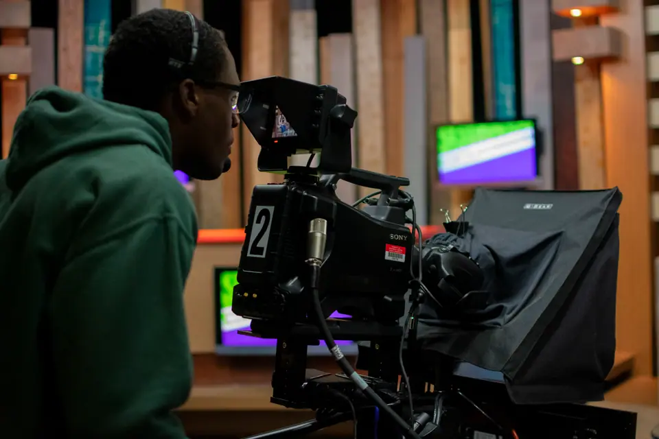 Camera operator lining up a shot behind a pedestal studio camera
