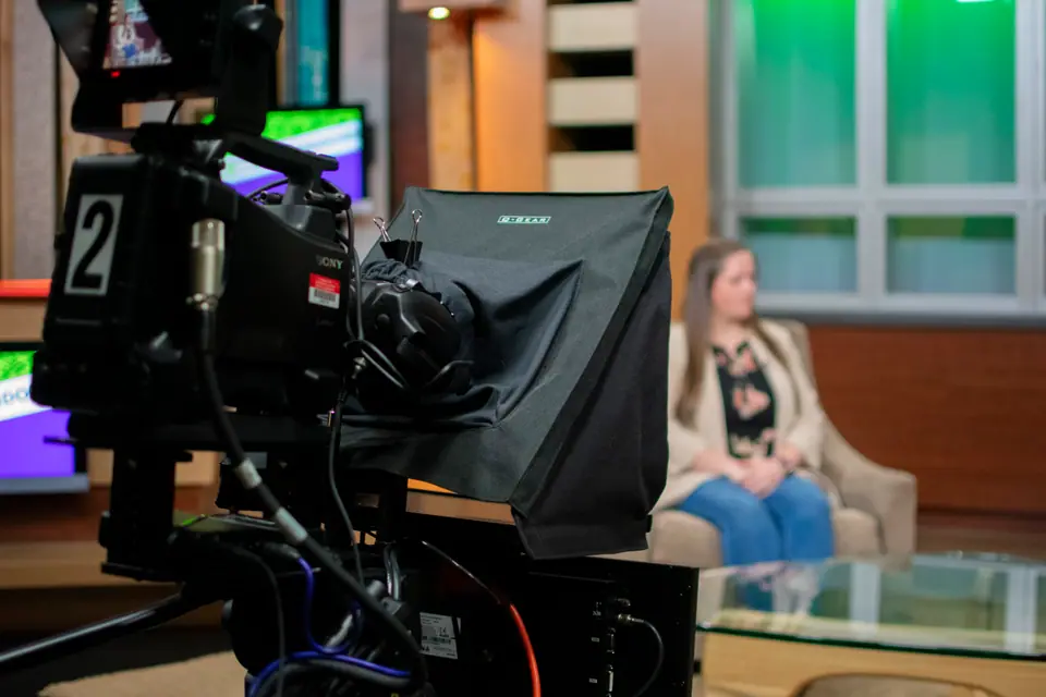 Studio camera marked two trained on a guest seated on the interview set