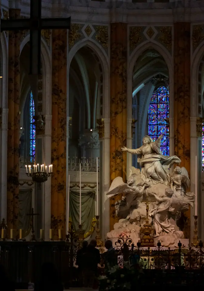 Carved marble altar group beneath stained glass, candles burning along the rail