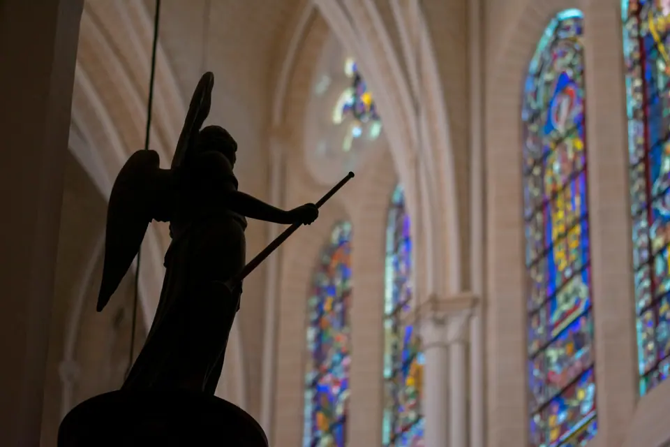 Winged angel statue silhouetted against stained-glass windows inside the cathedral