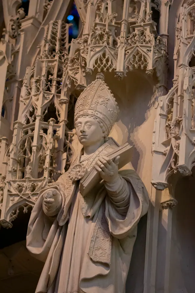 White stone statue of a mitred bishop standing in an ornately canopied niche