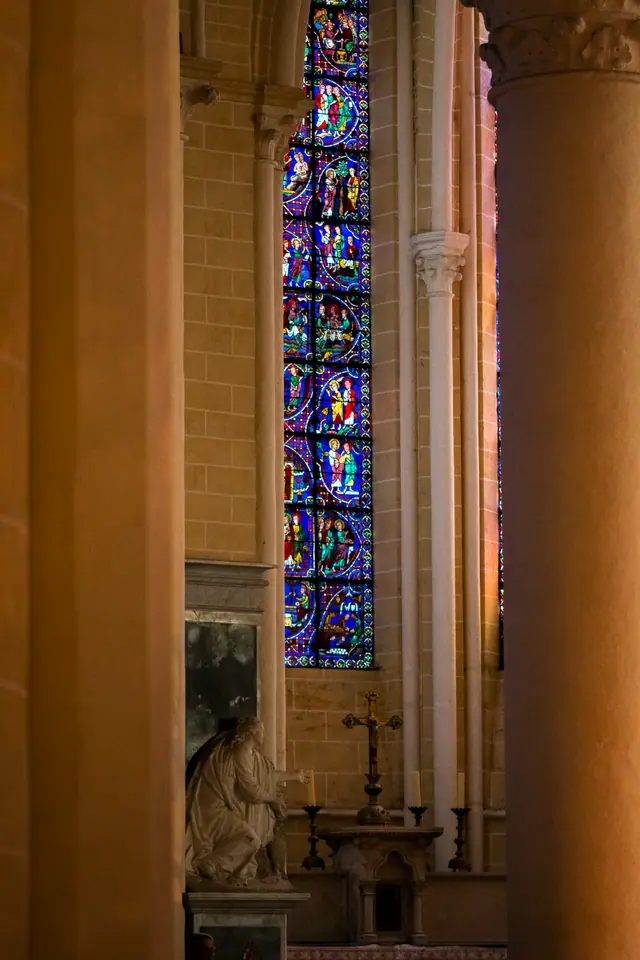 Cathedral column dividing a view of stained glass and a distant side altar