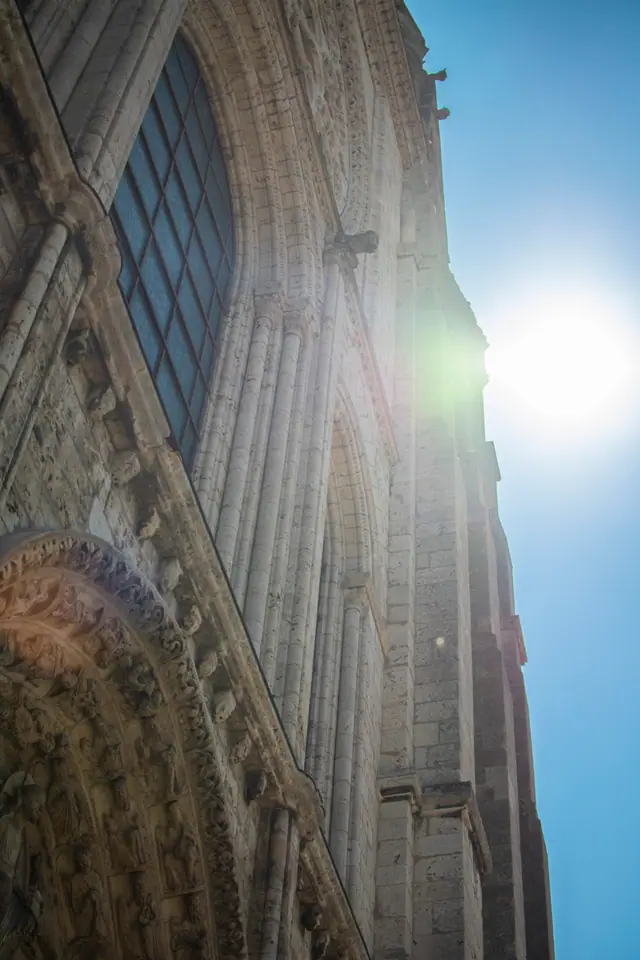 Chartres Cathedral's stone flank photographed into the sun, flare breaking across the buttresses