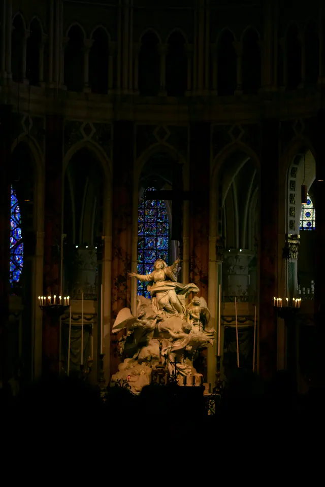 Dim cathedral interior with stained glass and a gilded sculptural group beyond the columns