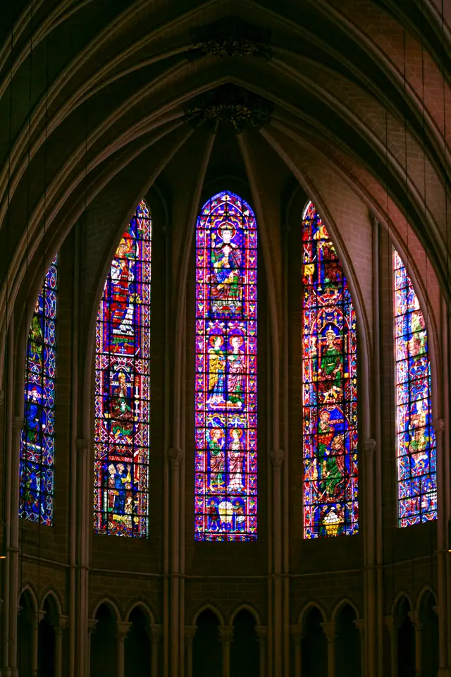 Three tall stained-glass lancet windows glowing blue and red in the cathedral wall