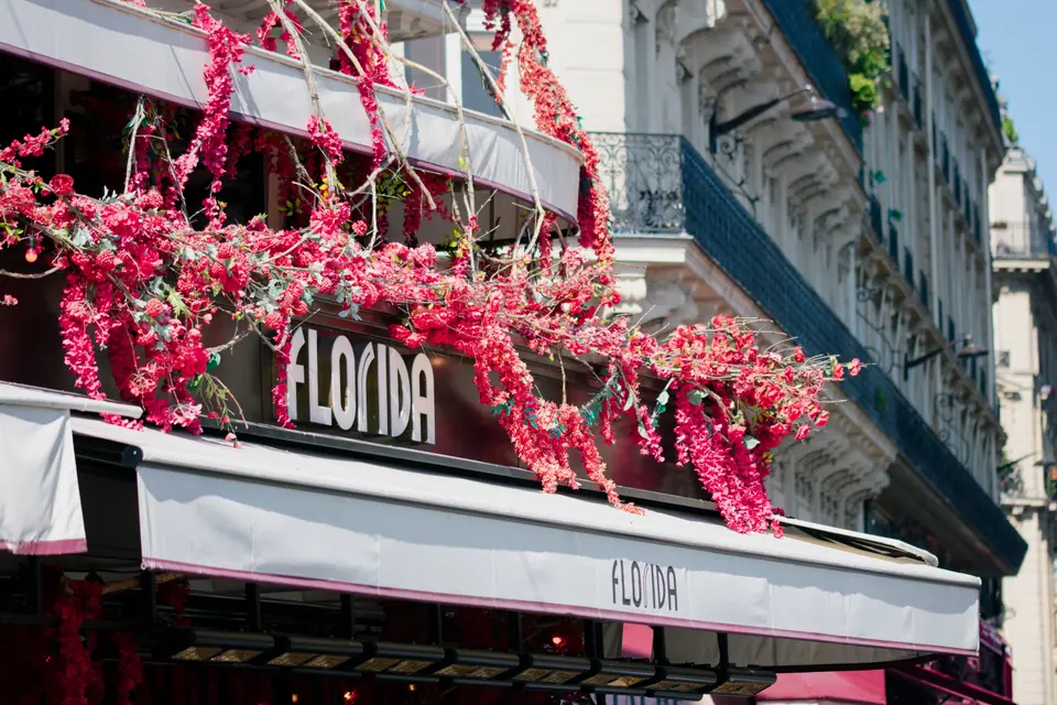 Travel & Architecture — Paris café front with white awnings and cascading pink blossom draped along the balcony above