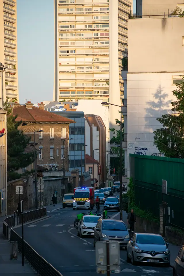 Steep Paris street busy with traffic, a tower block rising behind the older rooftops