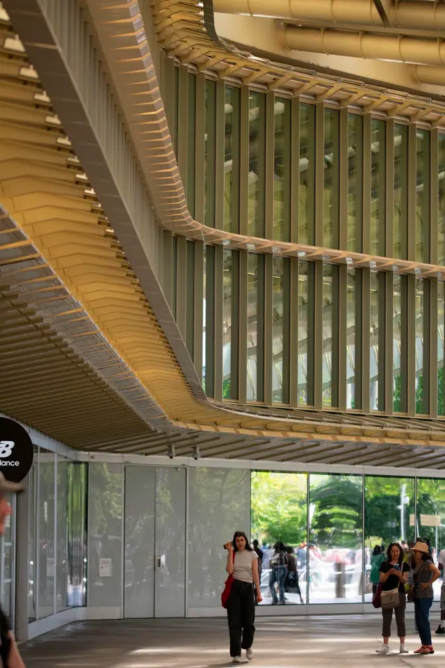 Underside of a curved modern building canopy, visitors walking through the glazed entrance below