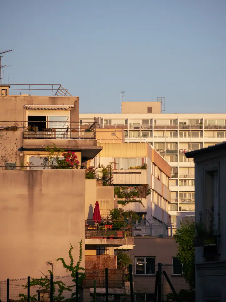 Paris apartment rooftops and terraces in golden evening light, a red parasol closed on a balcony