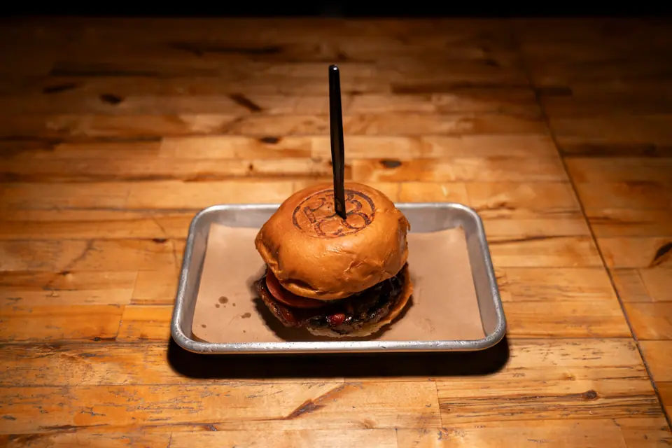 Burger with a branded toasted bun, centered on a metal tray on a wood table