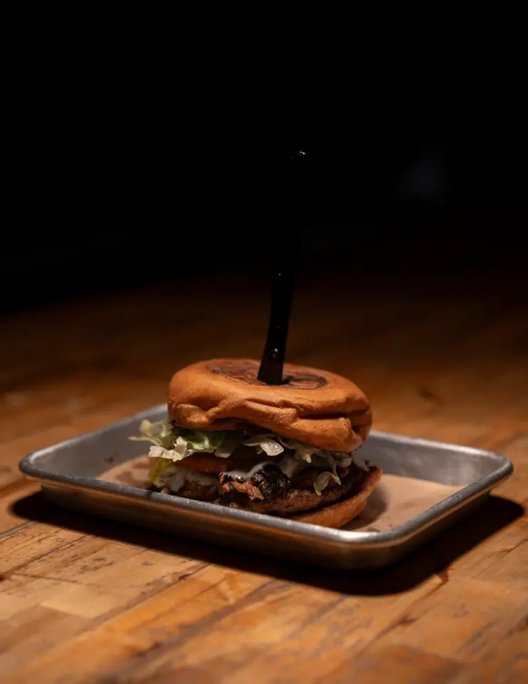 Double burger with a branded bun on a metal tray, lit from above