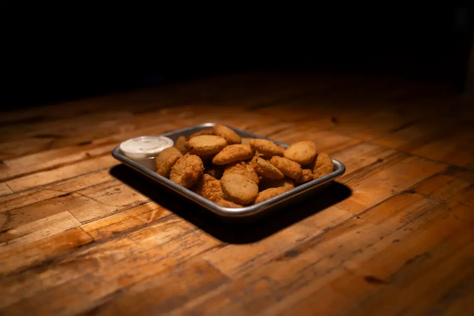 Fried appetizer bites with a cup of dipping sauce on a metal tray