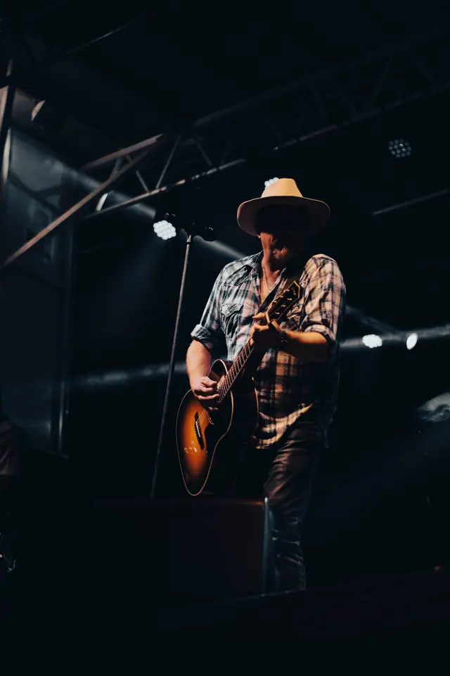Full-length view of a singer with an acoustic guitar on a darkened stage
