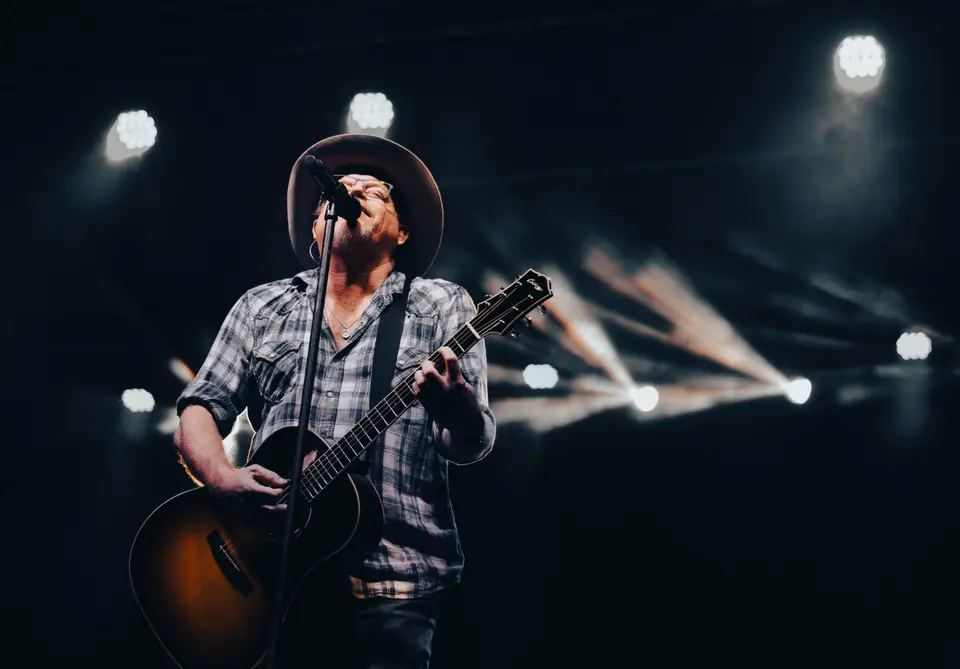 Singer leaning into the microphone mid-vocal, acoustic guitar in hand