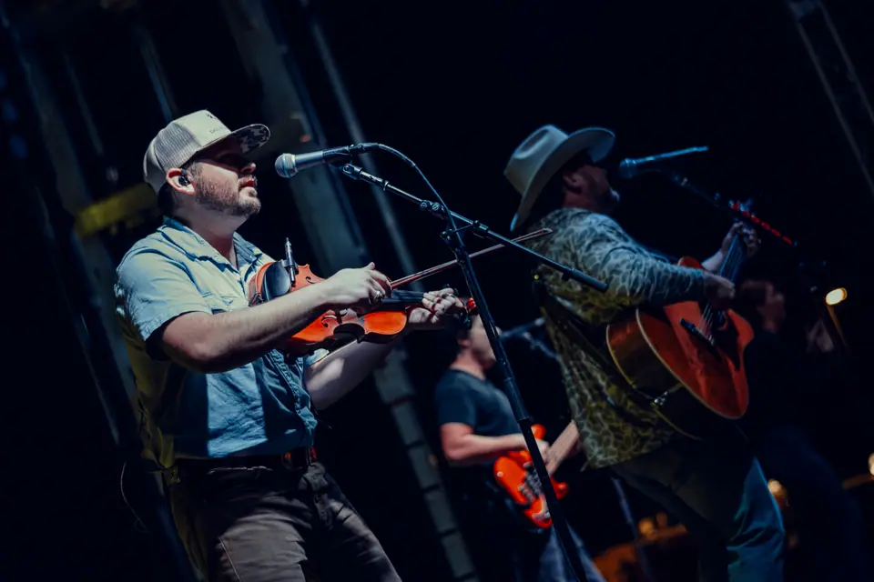 Fiddler in a cap and a guitarist sharing microphones at the front of a stage