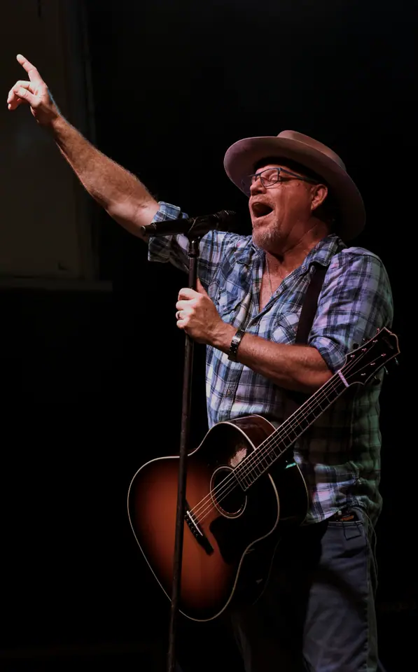Performer in a cowboy hat pointing out to the crowd while singing with a guitar
