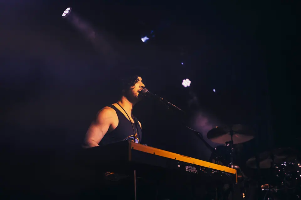 Singer performing at a keyboard, lit from behind in purple stage light