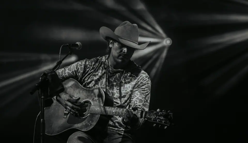 Black and white photograph of a singer in a cowboy hat playing acoustic guitar at the microphone