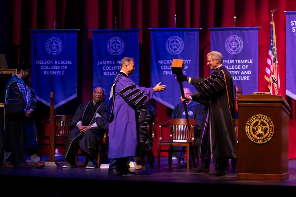 Two officials in academic robes greeting one another on stage during a university investiture