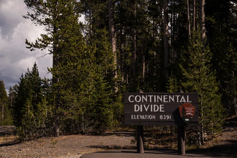 Roadside Continental Divide sign marking 8,391 feet, surrounded by tall pines