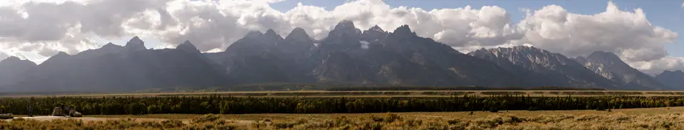 Panorama of the Teton range under heavy cloud, golden plain stretching across the foreground