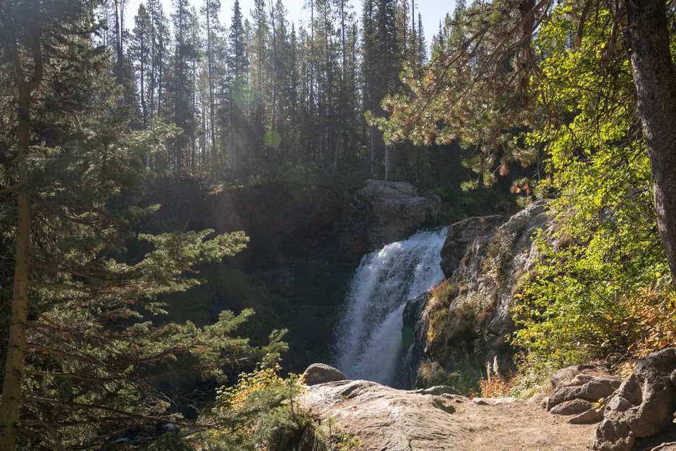 Waterfall spilling over dark rock into a pool ringed by pines and autumn scrub
