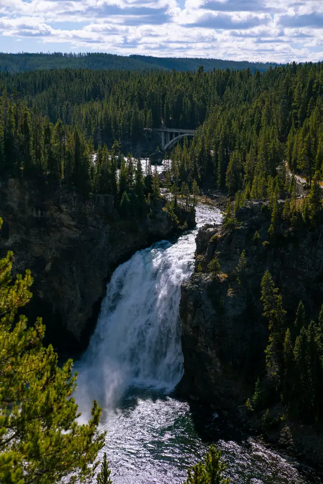 Large waterfall dropping into a forested canyon, pines lining both rims