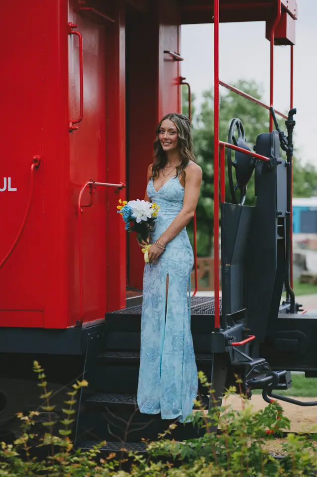 Young woman in a pale blue gown standing in the doorway of a red railroad caboose